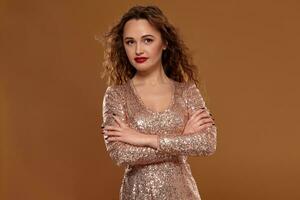 Portrait of young caucasian female in golden cocktail dress looking into the camera on brown background photo