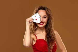 Pretty young brown-haired woman in red cocktail dress holding pair of aces and smiling photo