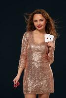 Brown-haired attractive caucasian young woman in golden cocktail dress at casino holds pair of aces and chips in her hands photo