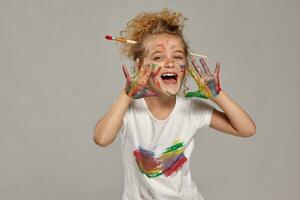 hermosa pequeño niña con un pintado manos y las mejillas es posando en un gris antecedentes. foto