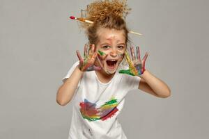 hermosa pequeño niña con un pintado manos y las mejillas es posando en un gris antecedentes. foto