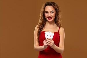 Pretty young brown-haired woman in red cocktail dress holding pair of aces and smiling photo