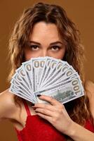 Image of lucky happy woman with brown long hair with fan of 100 dollar bills, lots of cash money, over brown background photo