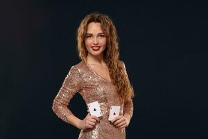 Pretty young brown-haired woman in golden cocktail dress holding pair of aces and smiling photo