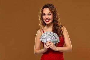 Image of lucky happy woman with brown long hair with fan of 100 dollar bills, lots of cash money, over brown background photo