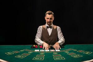 retrato de un crupier es participación jugando tarjetas, juego papas fritas en mesa. negro antecedentes foto