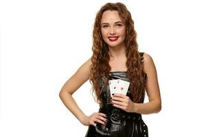 Pretty young redhead or brown-haired woman holding pair of aces in black leather dress isolated on white photo