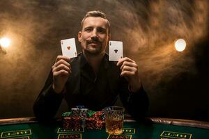 Man is playing poker with a cigar and a whiskey, a man show two cards in the hand, winning all the chips on the table with thick cigarette smoke. photo