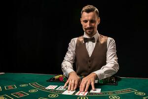 Portrait of a croupier is holding playing cards, gambling chips on table. Black background photo