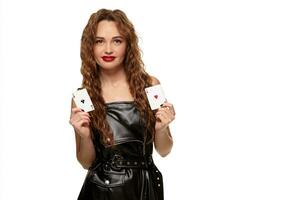 Pretty young redhead or brown-haired woman holding pair of aces in black leather dress isolated on white photo