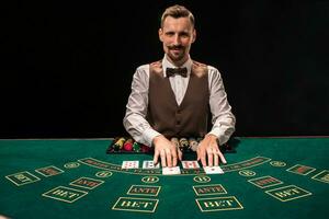 Portrait of a croupier is holding playing cards, gambling chips on table. Black background photo