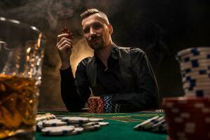 hombre es jugando póker con un cigarro y un whisky. un hombre victorioso todas el papas fritas en el mesa con grueso cigarrillo fumar. foto