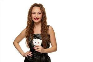 Pretty young redhead or brown-haired woman holding pair of aces in black leather dress isolated on white photo