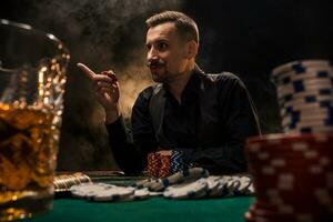 hombre es jugando póker con un cigarro y un whisky. un hombre victorioso todas el papas fritas en el mesa con grueso cigarrillo fumar. foto