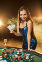 joven hermosa mujer poses cerca póker mesa en lujo casino. pasión, tarjetas, papas fritas, alcohol, dado, juego, casino - eso es como hembra entretenimiento. fumar antecedentes. foto