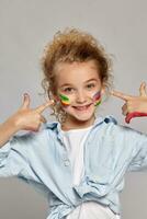 Beautiful little girl with a painted hands and cheeks is posing on a gray background. photo