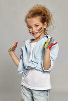 Beautiful little girl with a painted hands and cheeks is posing on a gray background. photo