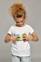 Beautiful little girl with a painted hands and cheeks is posing on a gray background. photo