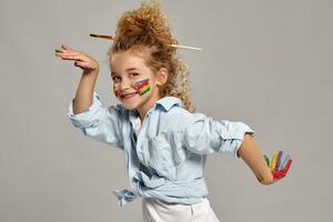 hermosa pequeño niña con un pintado manos y las mejillas es posando en un gris antecedentes. foto