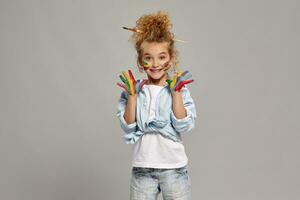 hermosa pequeño niña con un pintado manos y las mejillas es posando en un gris antecedentes. foto