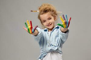 Beautiful little girl with a painted hands is posing on a gray background. photo