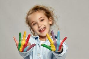 Beautiful little girl with a painted hands is posing on a gray background. photo