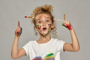 hermosa pequeño niña con un pintado dedos es posando en un gris antecedentes. foto