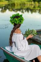 el ninfa con largo oscuro pelo en un blanco Clásico vestir sentado en un barco en el medio de el río. foto