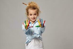 Beautiful little girl with a painted hands is posing on a gray background. photo