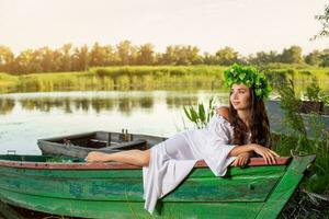 el ninfa con largo oscuro pelo en un blanco Clásico vestir sentado en un barco en el medio de el río. foto