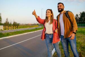 Happy couple hitchhiking on roadside trying to stop car. photo