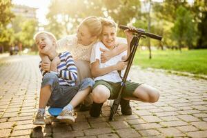 alegre madre teniendo divertido con su dos hijos en parque en soleado día. ellos son librar patineta y scooter. foto