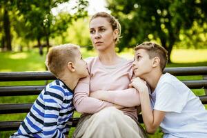 Mother is sitting with her sons on bench in park. She is angry and the boys try to apologize. photo