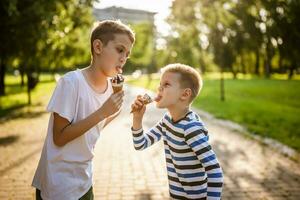 Two brothers are eating ice cream in park in summer. They are having fun and mocking at each other. photo