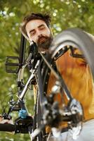 masculino ciclista sin prisa cheques y mantiene su bicicletas cadena en su hogar patio trasero. determinado joven caucásico hombre examinando bicicleta partes para daños y perjuicios a reparar para al aire libre ciclismo. foto