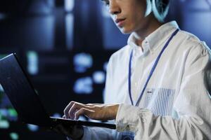 Dara center system administrator running code and programming on laptop, troubleshooting and upgrading high tech facility designed to accommodate rows of fully operational servers photo