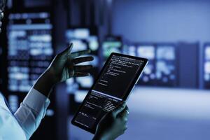 Close up of employee running code and programming on laptop, troubleshooting and upgrading high tech facility designed to accommodate multiple clusters of fully operational server hardware photo