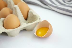 Fresh chicken eggs in a cardboard box and a broken egg on a white background. photo