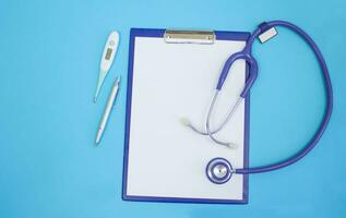 Stethoscope, tablet, pen and electric thermometer on a blue background. Copy space. photo