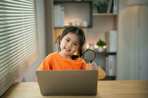 Asian baby kid girl holding magnifying glass and using laptop education to get good ideas, children and school concept - happy smiling student girl learning studying. Education development concept. photo