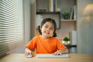 Asian baby girl wearing t-shirt smiling use laptop and study online on wood table desk in living room at home. Education learning online from home concept. photo