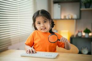 Asian baby kid girl holding magnifying glass and using laptop education to get good ideas, children and school concept - happy smiling student girl learning studying. Education development concept. photo