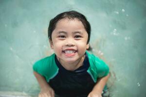 Asian child kid girl smiling funny wearing swimming suit to swimming or leaning training on swimming pool in water park. Water activity for children on summer holiday. photo