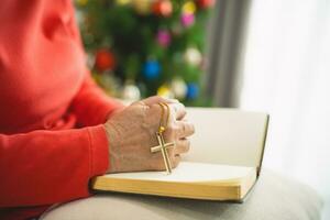 Close up hand. old senior woman doing hands together and  holding necklace of crosses prayer to God along with the bible In the Christian concept of faith, spirituality and religion. Christmas tree. photo