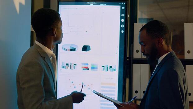 Teamworking businessmen working on company revenue statistical graphics in modern office during nightshift. Colleagues solving important project tasks, checking charts on digital screen photo