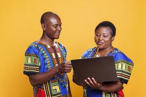 sonriente africano americano Pareja utilizando ordenador portátil y dando débito tarjeta información para en línea compra a verificar. alegre hombre y mujer en pie con portátil computadora y pago en Internet foto