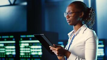 African american woman walking through server farm rows providing processing resources for different workloads. Admin fixing data center rackmounts tasked with solving complex operations photo