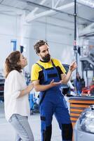 Expert in repair shop using AR technology to show customer car maintenance parameters. Garage worker using futuristic vr headset to inform client of what problems her vehicle is facing photo