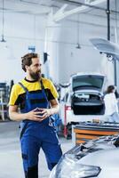 Engineer in repair shop using augmented reality holograms to check car specifications during checkup. Meticulous garage employee using futuristic AR technology to examine defective vehicle photo