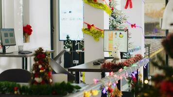 Empty festive ornate office with Christmas lights and garlands on walls. Financial graphs on computer screens in xmas adorn workplace with no employees during winter holiday season photo